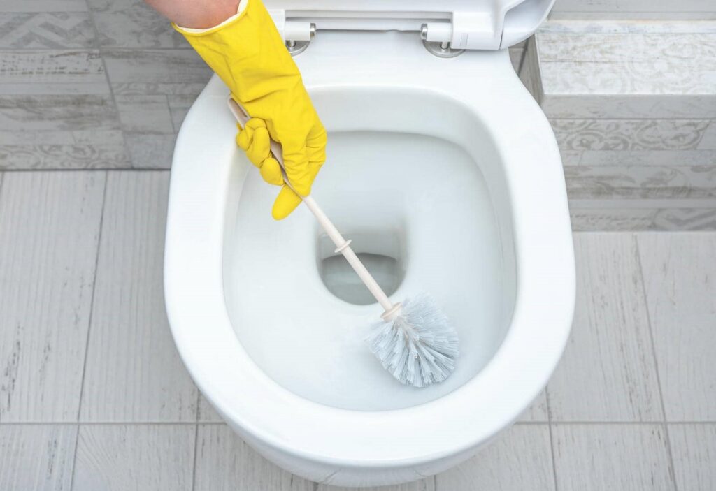 Hand in yellow glove cleaning a white toilet bowl with a brush.