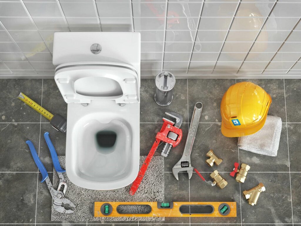 Toilet with plumbing tools, a yellow hard hat, and a towel arranged on a tiled floor.