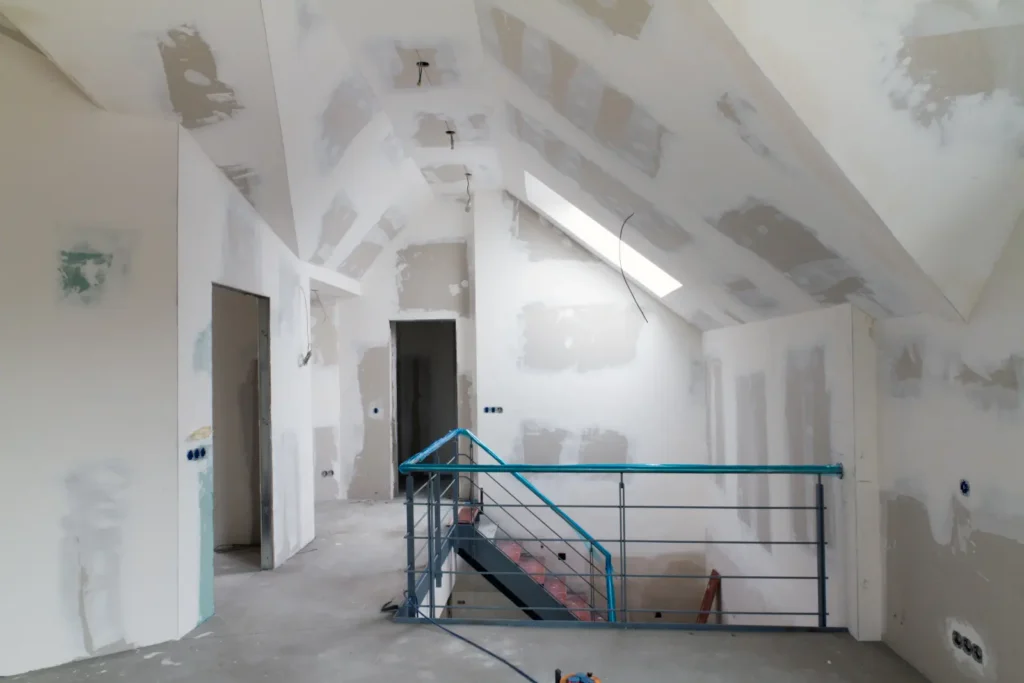 Unfinished attic hallway with drywall patches and a stair railing.